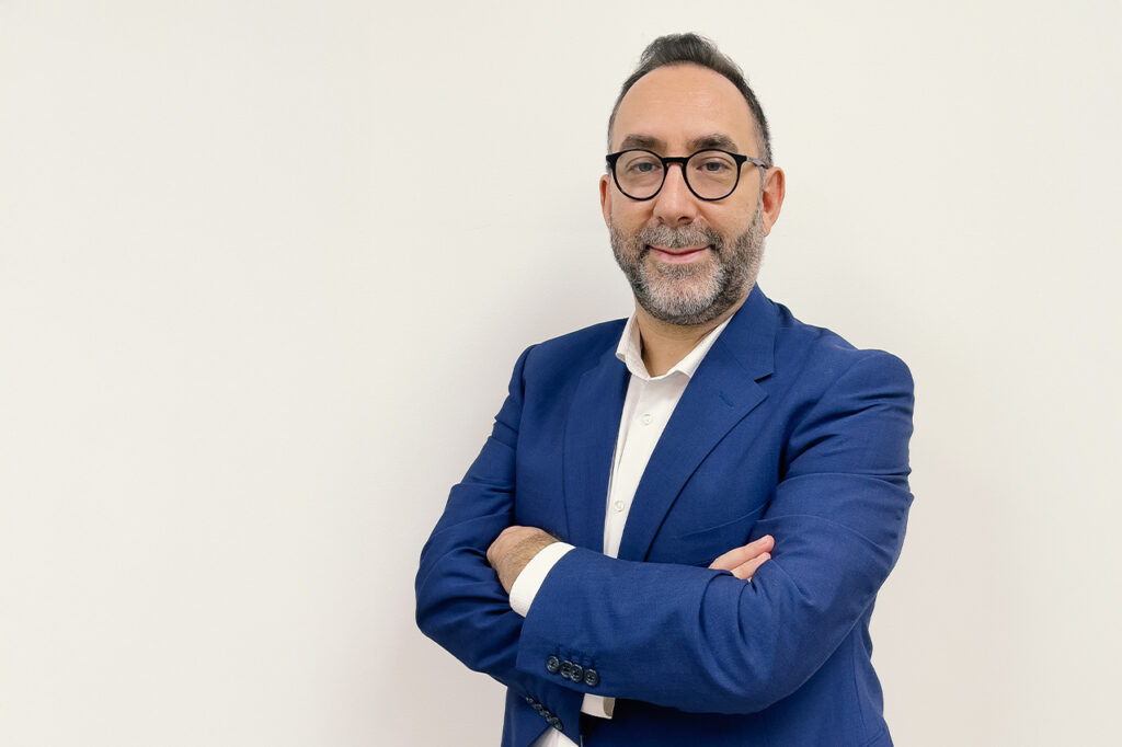 Ritratto di Andrea Palerma, CEO di Escogita, in posa con braccia conserte e sorriso, indossa un abito blu e camicia bianca