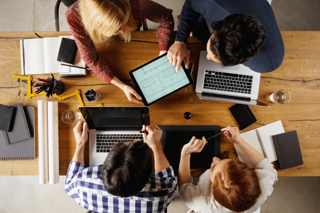 Gruppo di tecnici e progettisti riuniti attorno a un tavolo con planimetrie e computer portatili